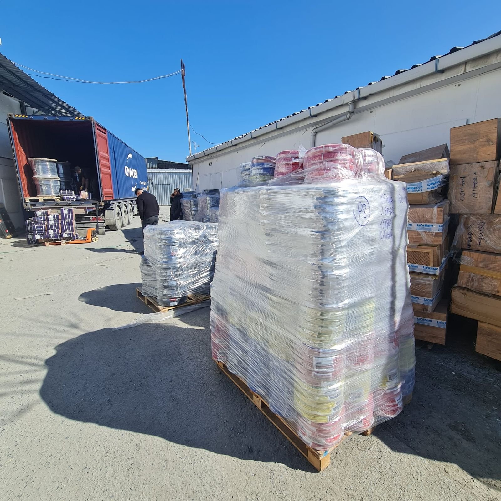 Wrapped pallets of cable reels beside an open shipping container at the TED yard
